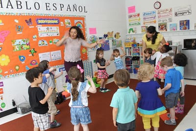 A SiW teacher leading a full class of preschoolers in Spanish under a "Hablo Español" classroom sign