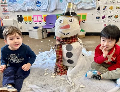 Two children sitting beside a snowman they built indoors during SiW winter camp