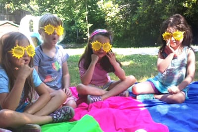 Four campers in sunflower sunglasses sitting on blankets outdoors at SiW summer camp