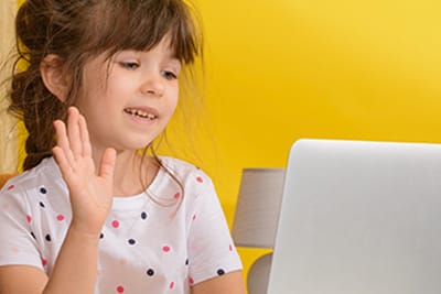 A young girl waving at her laptop during a live online Spanish class